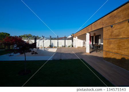 Modern villa with a private swimming pool and expansive wooden deck, featuring an outdoor dining area under a tiled roof. Enjoy luxurious living and relaxation in a beautiful, sunlit setting. 134575543