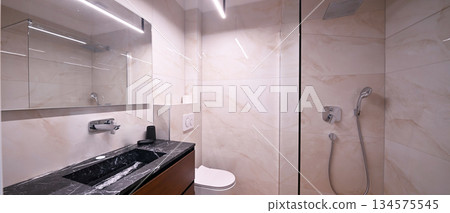 Luxurious modern bathroom featuring a sleek freestanding bathtub with a caddy, elegant vanity with sink and mirror, and a contemporary toilet. Soft tiled walls and wooden flooring create a spa-like Luxurious modern bathroom featuring a sleek freestanding bathtub with a caddy, elegant vanity with sink and mirror, and a contemporary toilet. Soft tiled walls and wooden flooring create a spa-like 134575545