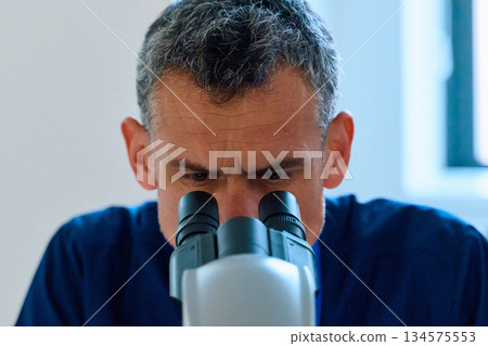 Microscopist examines samples in laboratory under bright lighting during the day Microscopist examines samples in laboratory under bright lighting during the day 134575553