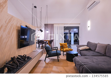 Modern open-plan living and dining area with an integrated kitchen, featuring a comfortable sofa, stylish armchairs, and a bar-height dining table. Wooden floors and ceiling beams enhance this Modern open-plan living and dining area with an integrated kitchen, featuring a comfortable sofa, stylish armchairs, and a bar-height dining table. Wooden floors and ceiling beams enhance this 134575585