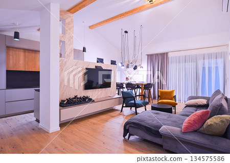 Modern open-plan living and dining area with an integrated kitchen, featuring a comfortable sofa, stylish armchairs, and a bar-height dining table. Wooden floors and ceiling beams enhance this Modern open-plan living and dining area with an integrated kitchen, featuring a comfortable sofa, stylish armchairs, and a bar-height dining table. Wooden floors and ceiling beams enhance this 134575586