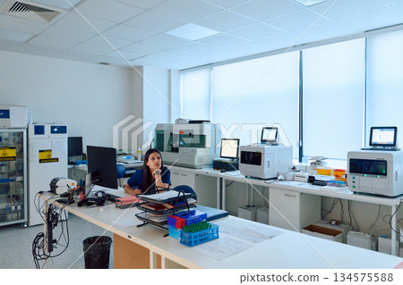 Laboratory setting featuring a female scientist engaged in research work amid advanced equipment and a clean workspace during daylight hours 134575588