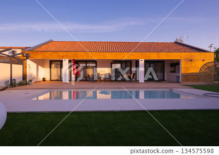 Modern villa with a private swimming pool and expansive wooden deck, featuring an outdoor dining area under a tiled roof. Enjoy luxurious living and relaxation in a beautiful, sunlit setting. Modern villa with a private swimming pool and expansive wooden deck, featuring an outdoor dining area under a tiled roof. Enjoy luxurious living and relaxation in a beautiful, sunlit setting. 134575598