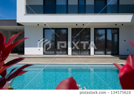 Modern luxury villa with swimming pool and clean minimalist architecture under a blue sky. Contemporary residential exterior featuring large windows, terrace, and elegant outdoor living space 134575628