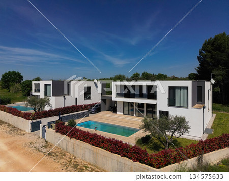Aerial view of two stunning modern luxury villas with private swimming pools, elegant architecture, and lush green landscaping, set against a beautiful natural backdrop Aerial view of two stunning modern luxury villas with private swimming pools, elegant architecture, and lush green landscaping, set against a beautiful natural backdrop 134575633
