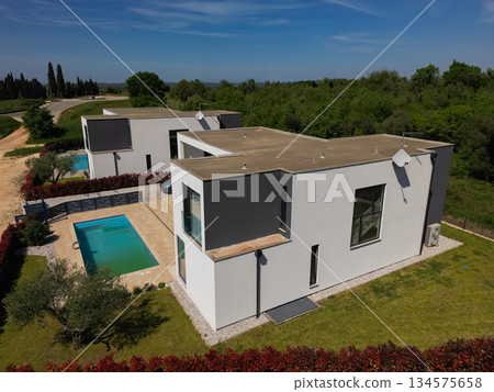 Aerial view of two stunning modern luxury villas with private swimming pools, elegant architecture, and lush green landscaping, set against a beautiful natural backdrop Aerial view of two stunning modern luxury villas with private swimming pools, elegant architecture, and lush green landscaping, set against a beautiful natural backdrop 134575658
