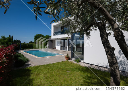 Modern luxury villa with swimming pool and clean minimalist architecture under a blue sky. Contemporary residential exterior featuring large windows, terrace, and elegant outdoor living space 134575662