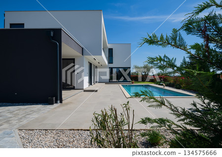 Modern luxury villa with swimming pool and clean minimalist architecture under a blue sky. Contemporary residential exterior featuring large windows, terrace, and elegant outdoor living space 134575666