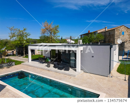 Aerial view of a modern modular house with flat roof, swimming pool, and patio. Contemporary prefabricated home architecture featuring sustainable design and outdoor living space Aerial view of a modern modular house with flat roof, swimming pool, and patio. Contemporary prefabricated home architecture featuring sustainable design and outdoor living space 134575674