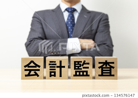 一位商人雙手交叉放在胸前，手裡拿著一塊寫著「審計」字樣的積木。 134576147