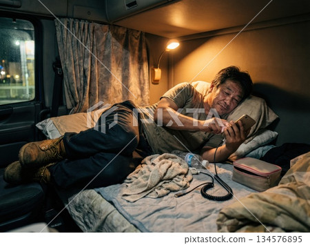 一名長途卡車司機在夜間休息時在卡車裡使用智慧型手機 134576895