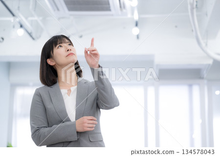 A business woman is confused about the company's air conditioning and equipment inspection and is thinking about equipment maintenance. She points to the air conditioner. 134578043