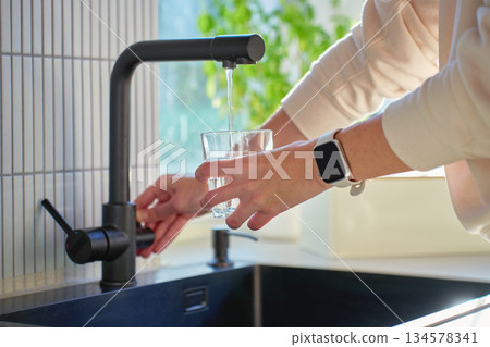 Hand filling glass with drinking water from kitchen faucet Hand filling glass with drinking water from kitchen faucet 134578341