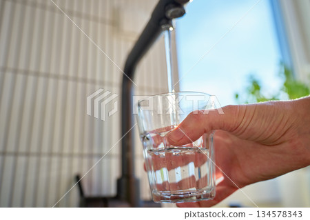 Glass filled with clear water from black kitchen faucet in daylight 134578343
