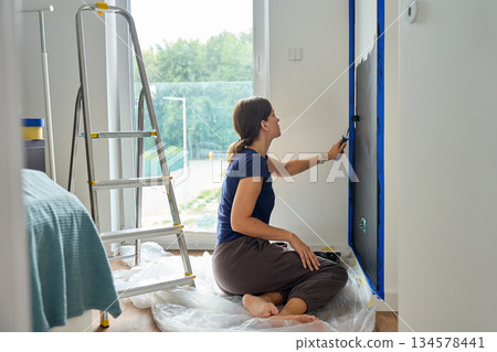 Woman painting wall with roller during home renovation 134578441