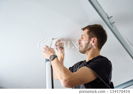 Man connecting electrical wires while installing ceiling light indoors Man connecting electrical wires while installing ceiling light indoors 134578459