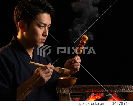 Japanese male craftsman in kimono grilling mitarashi dango over charcoal 134578544