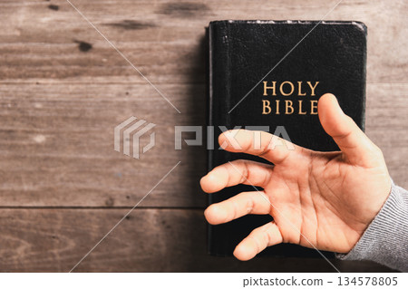 Hands in prayer above Holy Bible on wooden table, symbolizing Christian faith, worship, devotion, trust in God, spiritual religious background with copy space for church, prayer, meditation concepts. 134578805