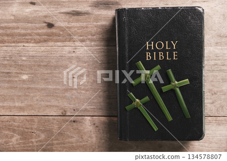 Holy Bible, three palm leaf crosses placed on over wooden table, symbolizing Christian faith, Palm Sunday, worship, spiritual devotion, religious background with copy space for church design. 134578807
