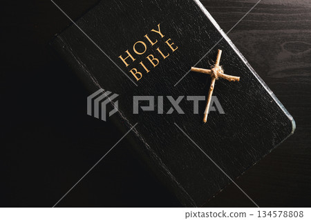 Holy Bible small wooden cross placed black leather cover dark dramatic light symbolizing Christian faith belief worship devotion religion background copy space for church prayer spiritual concept 134578808