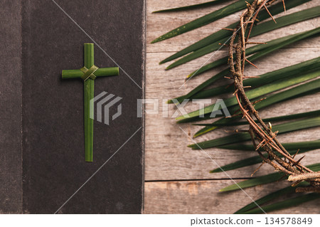 Palm leaves cross with crown of thorns, palm leaves beside Bible on rustic wooden table, symbolizing Christian faith, sacrifice, Palm Sunday, Easter reflection, religious background for worship. Palm leaves cross with crown of thorns, palm leaves beside Bible on rustic wooden table, symbolizing Christian faith, sacrifice, Palm Sunday, Easter reflection, religious background for worship. 134578849