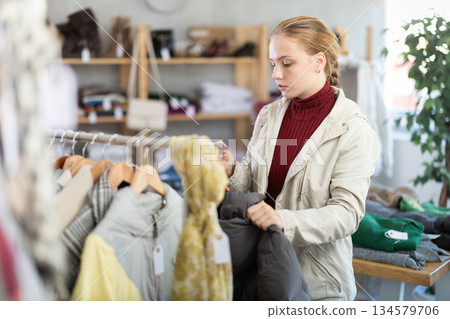 While shopping, teen girl browsing goods items and choose elect down jacket in store 134579706