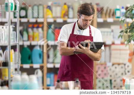 Male employee, with tablet in hands, make inventory in store. Male employee, with tablet in hands, make inventory in store. 134579719