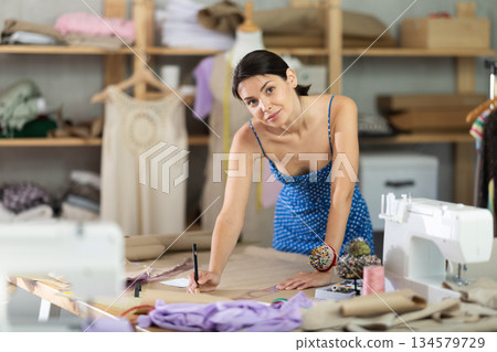 Woman seamstress drawing pattern on paper in workshop Woman seamstress drawing pattern on paper in workshop 134579729