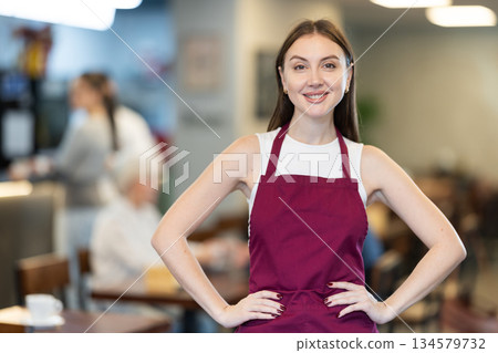 Female barista standing in front of interior background in cafe Female barista standing in front of interior background in cafe 134579732