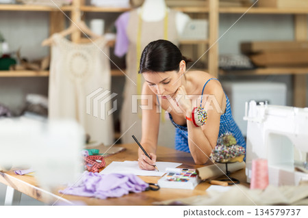 Young woman seamstress draws sketch on paper Young woman seamstress draws sketch on paper 134579737
