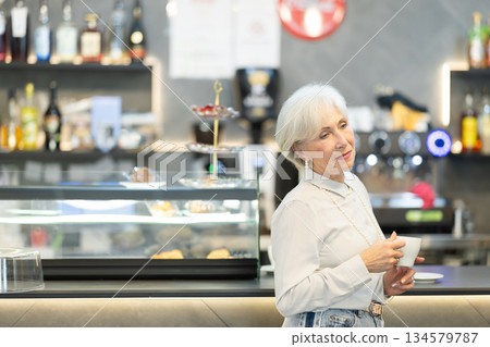 Elderly woman drinking coffee at a table in a cafe Elderly woman drinking coffee at a table in a cafe 134579787