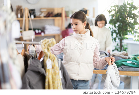 Teen girl looks at products in store and selects coat or jacket. Family shopping 134579794