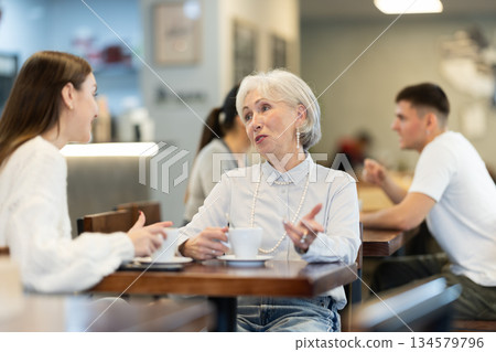 Mature woman and her adult daughter sit together at table in cafe 134579796