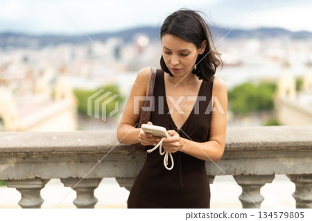 Young woman standing on street with mobile in her hands 134579805