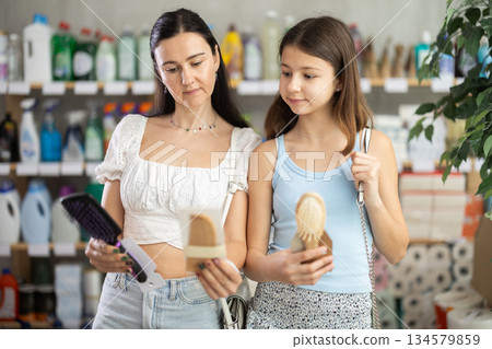 Preteen girl with mother choosing hair brushes in toiletries store 134579859