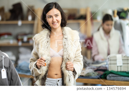 Woman try on fur jacket in front of mirror in clothes store, semi naked body Woman try on fur jacket in front of mirror in clothes store, semi naked body 134579894
