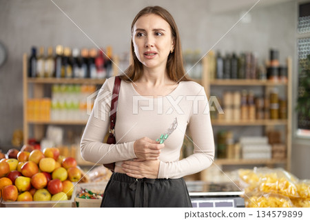 Woman develops stomach ache while grocery shopping in supermarket Woman develops stomach ache while grocery shopping in supermarket 134579899