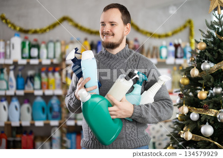 Cheerful customer holding cleaning an personal care products in Christmas decorated store Cheerful customer holding cleaning an personal care products in Christmas decorated store 134579929