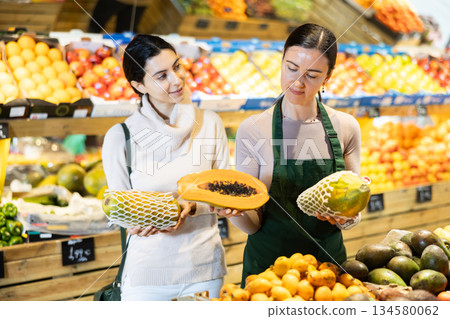 Woman shop assistant accompanies customer, help to choose papaya 134580062