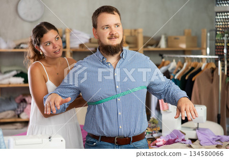 Seamstress measuring client in sewing studio for custom garment Seamstress measuring client in sewing studio for custom garment 134580066