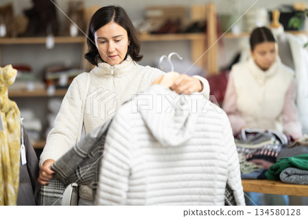 Adult woman chooses coat or down jacket in clothing store Adult woman chooses coat or down jacket in clothing store 134580128