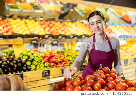 Middle-aged female seller putting tomatoes on counter in grocery market 134580133