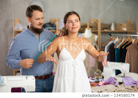 Fashion designer measuring female client for tailored clothing 134580174