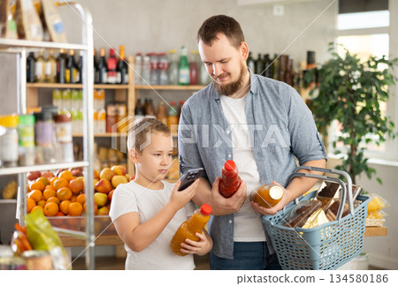 European man with son customer at shop scans QR code on juice bottle using phone camera 134580186