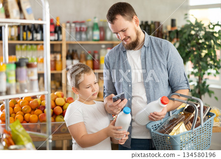 European man with son customer at shop scans QR code on milk bottle using phone camera European man with son customer at shop scans QR code on milk bottle using phone camera 134580196