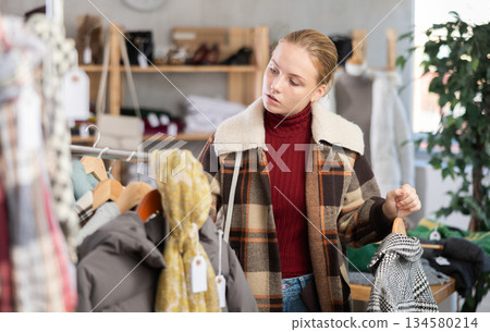 While shopping, teen girl browsing goods items and choose elect something warm outerwear in store 134580214