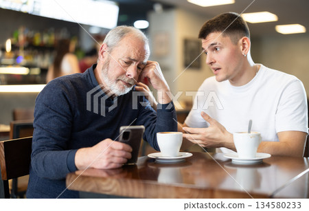 Young and elderly man with phone in cafe Young and elderly man with phone in cafe 134580233