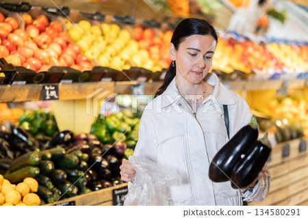 Female shopper carefully selecting ripe zucchini in supermarket 134580291