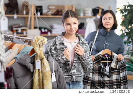 Teenage girl with her mother try on coat in store Teenage girl with her mother try on coat in store 134580298