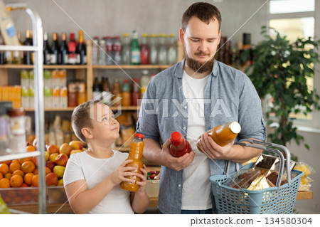 Preteen boy with father choosing juices in bottles in supermarket 134580304